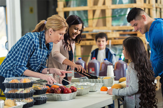 Volunteers serve meals to a man and young girl