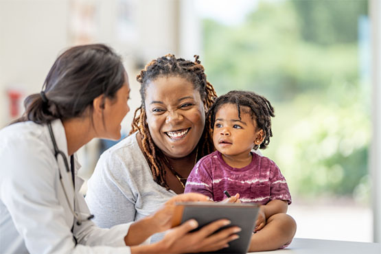 A mother with young child laughs with a pediatric healthcare provider