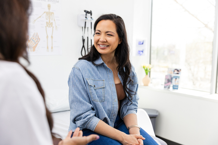 A smiling woman sits on a medical provider examination table