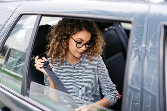 A woman in the backseat of a car buckles her seatbelt